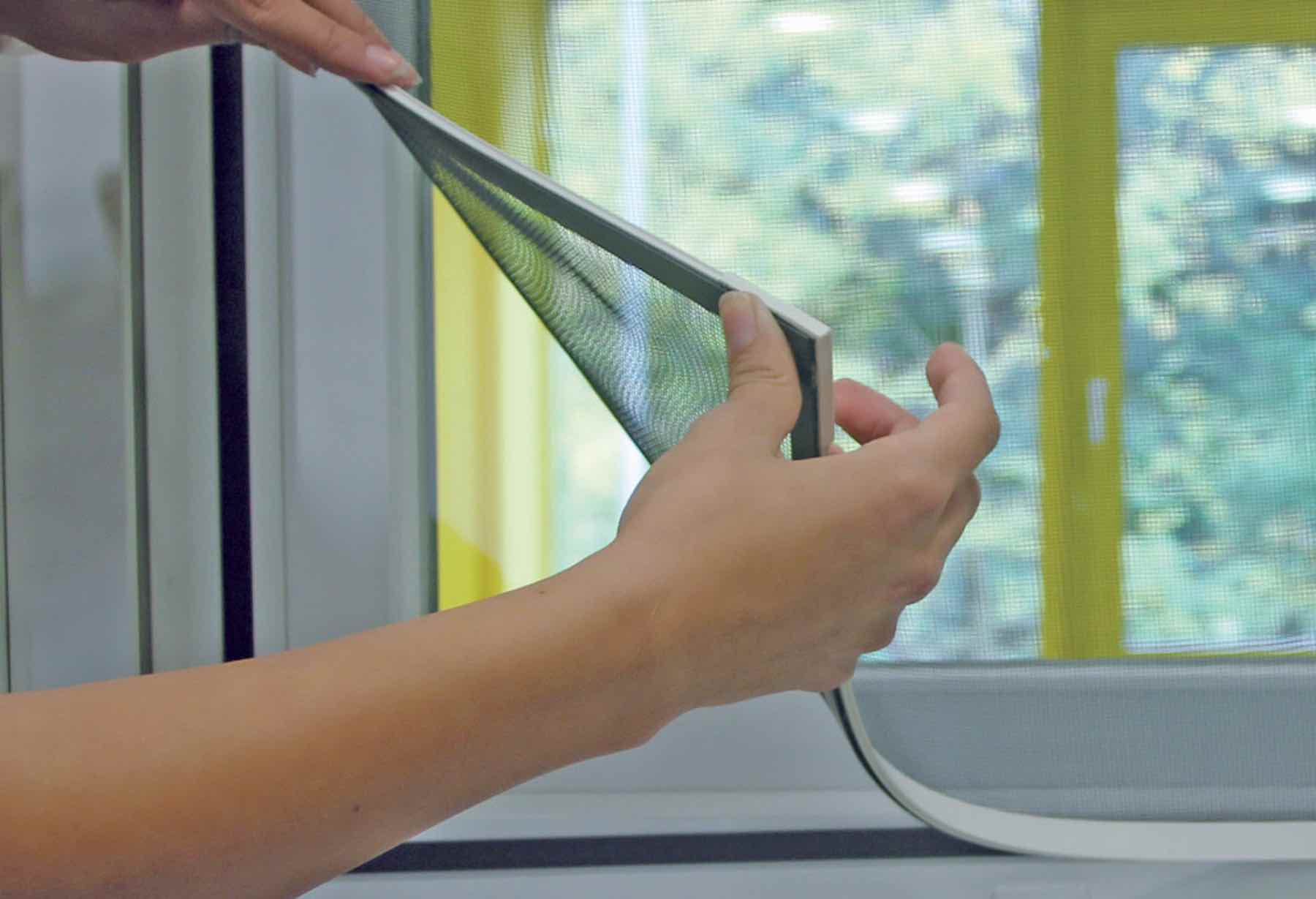 Dalawang kamay na inaangat ang magnetic window screen mula sa magnetic strip sa frame ng bintana